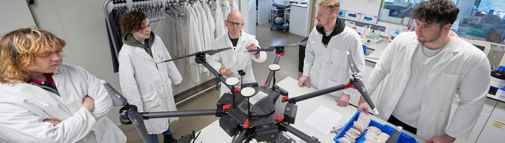 Small group of students looking at a drone in the lab