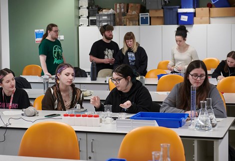 Two groups of students working at benches with various containers on the bench