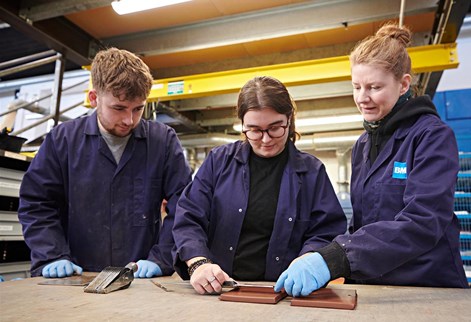 Two students on placement working with a colleague measuring tile samples in a workshop