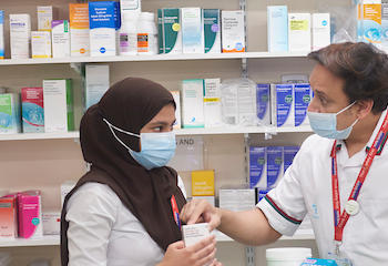 Male and female standing in front of shelf with medicines