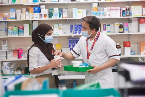 Male and female standing in front of shelf with medicines