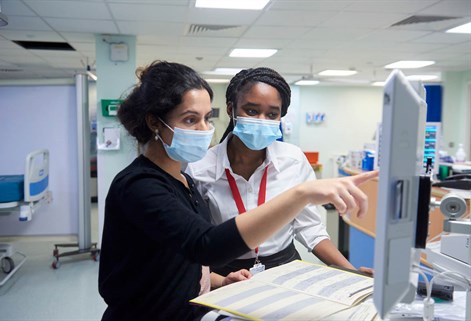 Two females in a hospital setting looking at a screen and notes