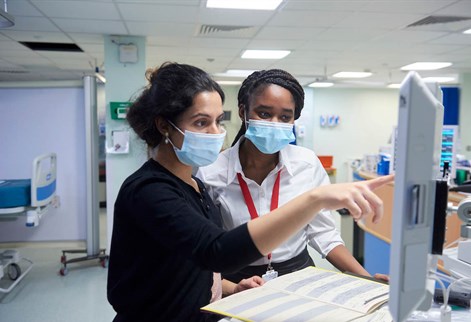 Two females in a hospital setting looking at a screen and notes