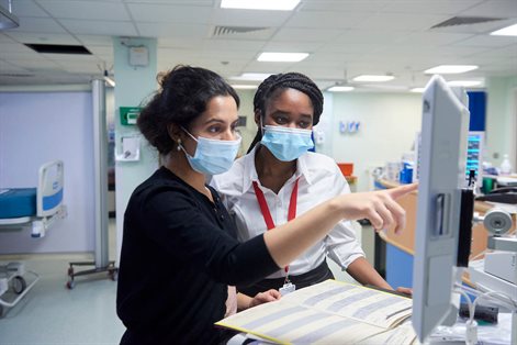 Two females in a hospital setting looking at a screen and notes