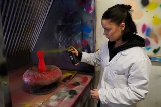 Female product design student spraying object in spray booth