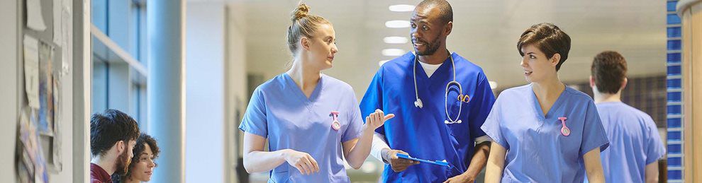 Three people in medical scrubs chatting as they walk down a corridor