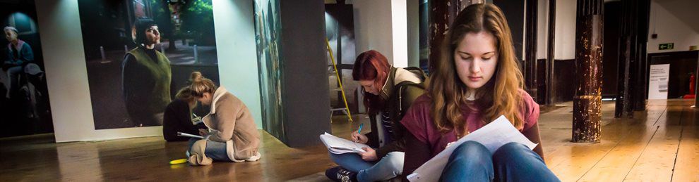 Students sitting on the floor of a gallery making notes