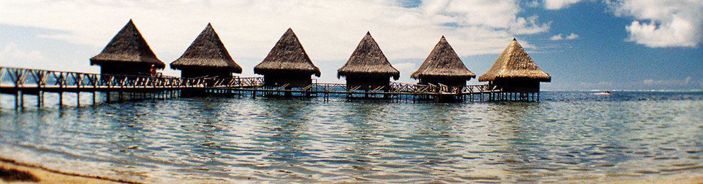 Six huts on stilts linked by a walkway located on a beach abroad