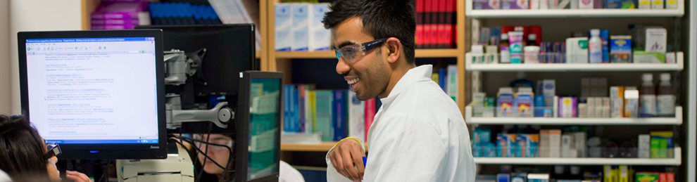 Pharmacy students in white coats by a computer screen