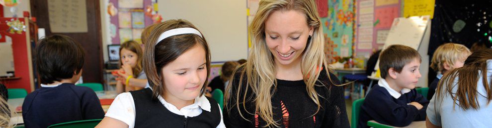 Smiling primary school teacher with children in the classroom.
