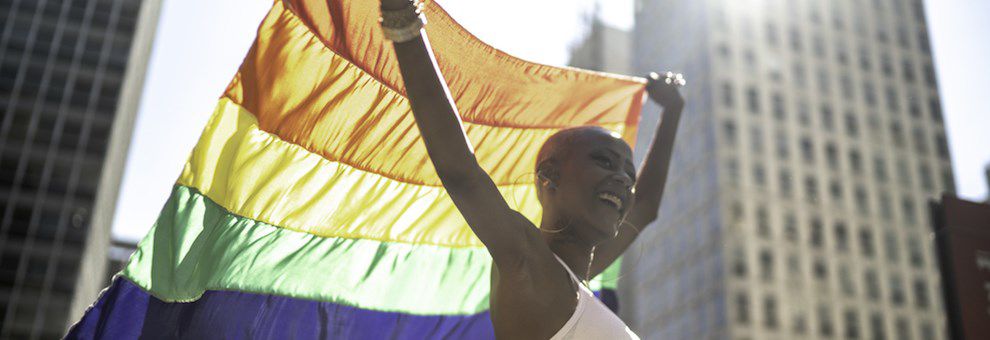 A black woman holding a rainbow flag above her head