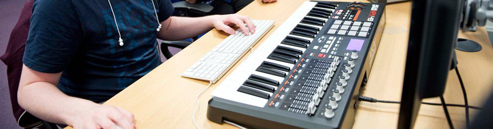 Close up of a student's hands on a desk with a computer keyboard and a musical keyboard