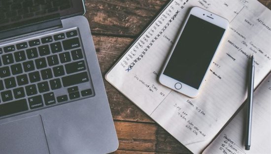 A desk with a laptop, phone and notepad