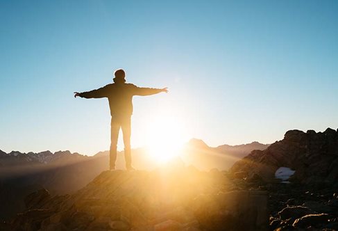 Someone standing with their arms out looking at a sunrise