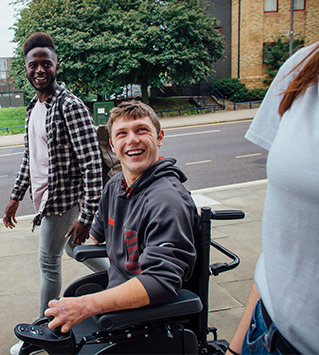 Three friends walking down the street together, one is using a wheelchair.