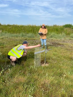 Estury wetlands and two researchers conducting experiment to record surface elevation at the Adur Estuary, England
