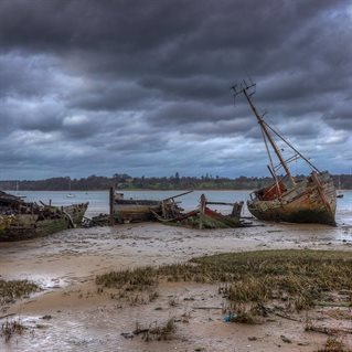 Harbour with beach and grey cloud. Abandoned boats in Chichester harbour, England