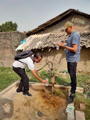 Two aquatic researchers using a standpipe outside roughly constructed buildings. Collection of household stored water in Terai, Nepal