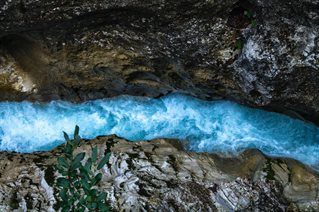 Birds eye view down both sides of rocky chasm with fast moving blue river below. Courtesy Jonas Gerg and Unsplash
