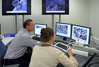 Biomedical researchers seated at a desk with multiple screens showing electronic microscopic views of biomedical tissue samples