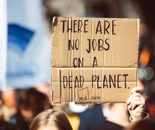 A cardboard, handwritten sign on a protest march reads No jobs on a dead planet. Representing applied philosophy and ethics research.