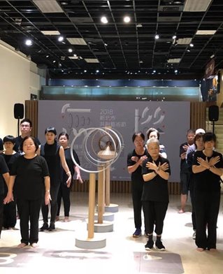 A group of twenty Taiwanese museum workers dressed in black stand in rows around sculptures in the museum
