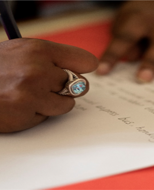 Hands writing on a sheet of paper with a pencil as part of Clothes on our backs, a Minority Ethnic community writing project