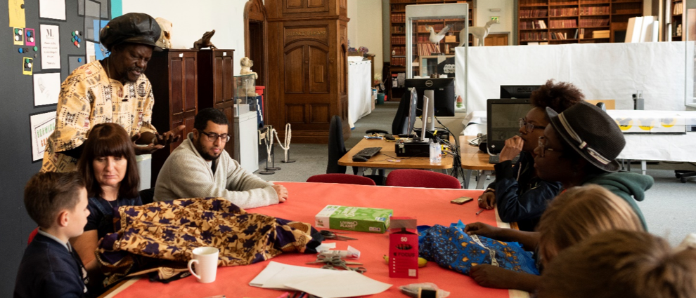 A mixed age group in a museum setting share stories of black and ethnic minority origins using cloth and textile props and writing materials