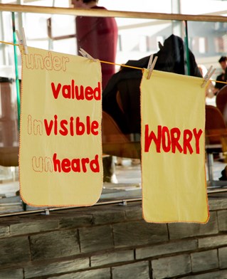 Yellow dusters embroidered with words 'invisible' 'unheard' supporting carers' activism at the Senned Cymru