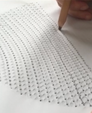 Artist's hands working with a pencil puncturing a piece of paper in geometric design