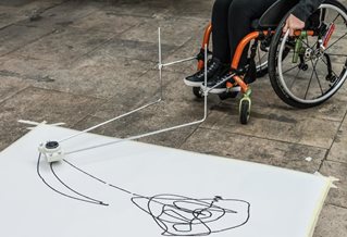 Wheels of wheelchair and large paper onto which wheelchair user draws using specially constructed equipment