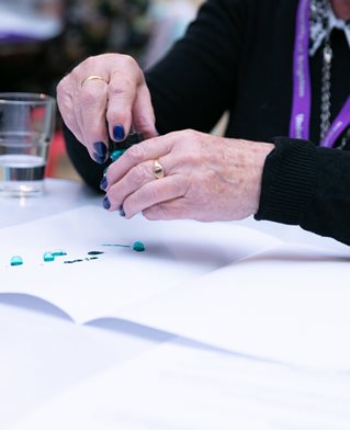 Elderly hands work with green ink to make drop and bubble marks on paper