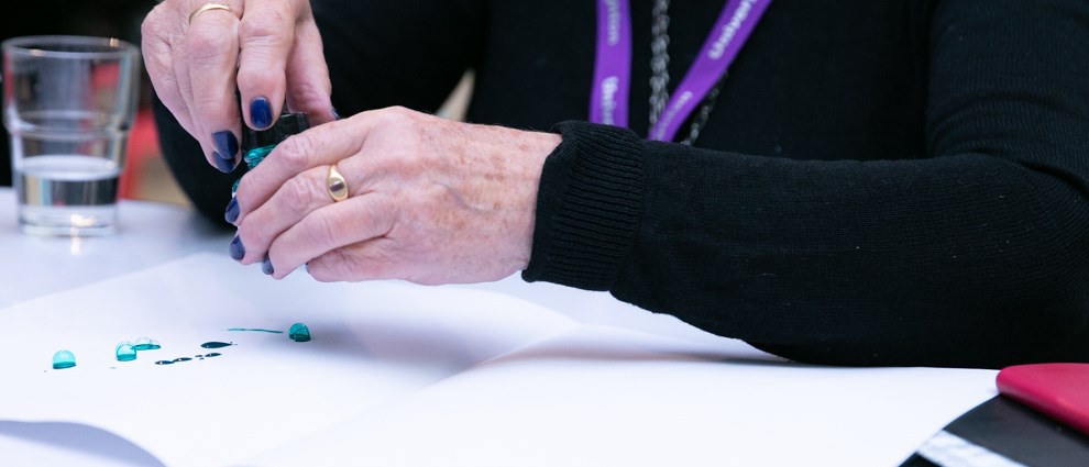 Elderly hands work with green ink to make drop and bubble marks on paper