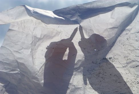 Artist Jane Fox's hands visible in silhouette and shadow through a crinkled white cloth making marks on the wind-blown material