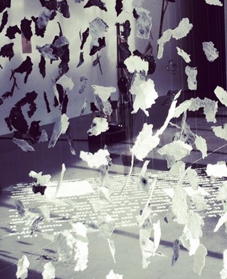 Installation by Jules Findlay, pieces of torn paper cascade from the gallery ceiling, picked out by light from the nearby window