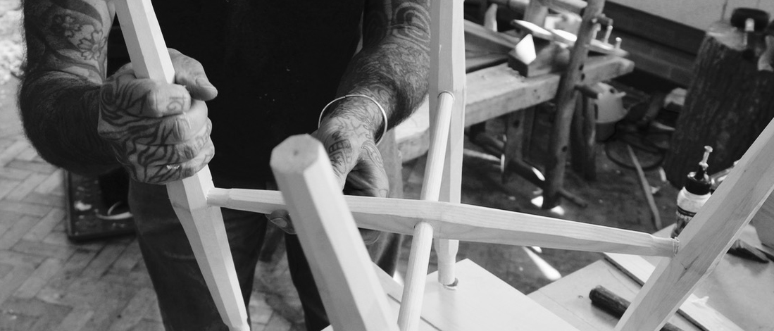 Black and white image of person constructing the underside of a wooden chair.