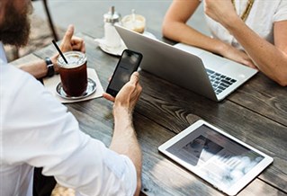 Two people meeting for coffee with a phone, laptop and tablet