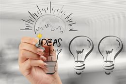 Graphic of hand reaching for a lightbulb on which is written the word ideas. Symbolising innovation and entrepreneurship in management studies.