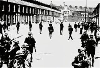 Black and white photograph of soldiers carrying guns and wearing metal helmets. They stand in a wide street of terrace housing.