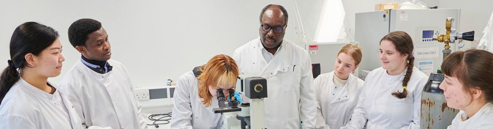 Student in genomics lab looking through microscope surrounded by students