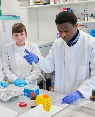 Two laboratory genomic research scientists in white coats and blue gloves with sampling equipment