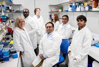 Seven precision medicine researchers seated and standing in white coats for photograph in University of Brighton Genomics Lab
