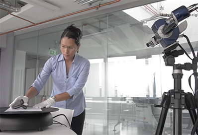 A researcher in white gloves placing an object on a circular stand in front of a camera for 3D modeling.