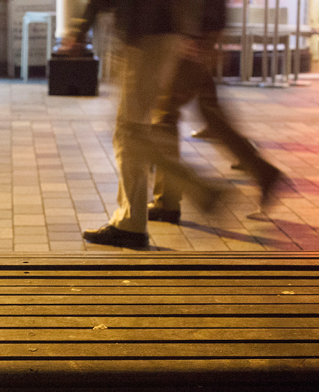 Photograph of moving legs passing a station bench