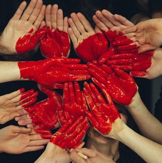 Several pairs of hands held up with a painted red heart symbol. Courtesy Unsplash Tim Marshal.