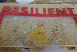 A paint-splattered board with the word 'Resilient' made out of plasticine depicting resilience research with children.