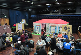 A group of people sitting in a community hall with brightly coloured posters around them in a resilience workshop.