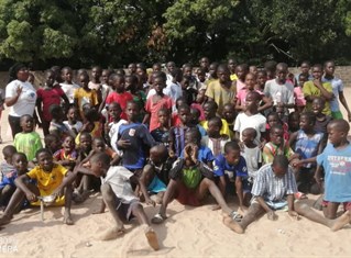 Large group of children of different ages gather on a beach in The Gambia, participants in Football 4 Peace.