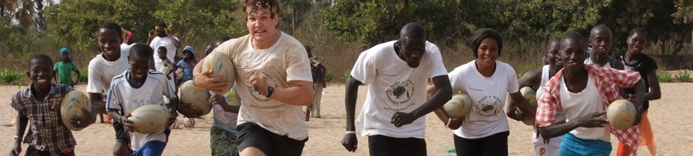 Group of boys and men running towards the camera across a beach, one with a rugby ball. Rugby 4 Peace.