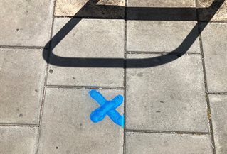 Blue street graffiti of an X on the pavement and sharp shadow line from railing